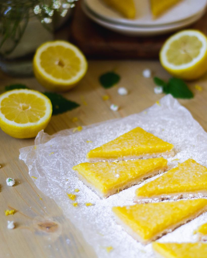Triangular cuts of lemon bars on a crinkled sheet of wax paper showing a bright yellow lemon custard filling dusted with powdered sugar.
