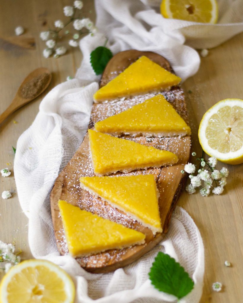 Triangular cuts of lemon bars on a wooden cutting board showing bright yellow lemon custard filling dusted with powdered sugar.