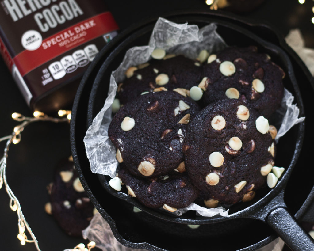 dark chocolate cookies in a cast iron skillet with cocoa powder in the background