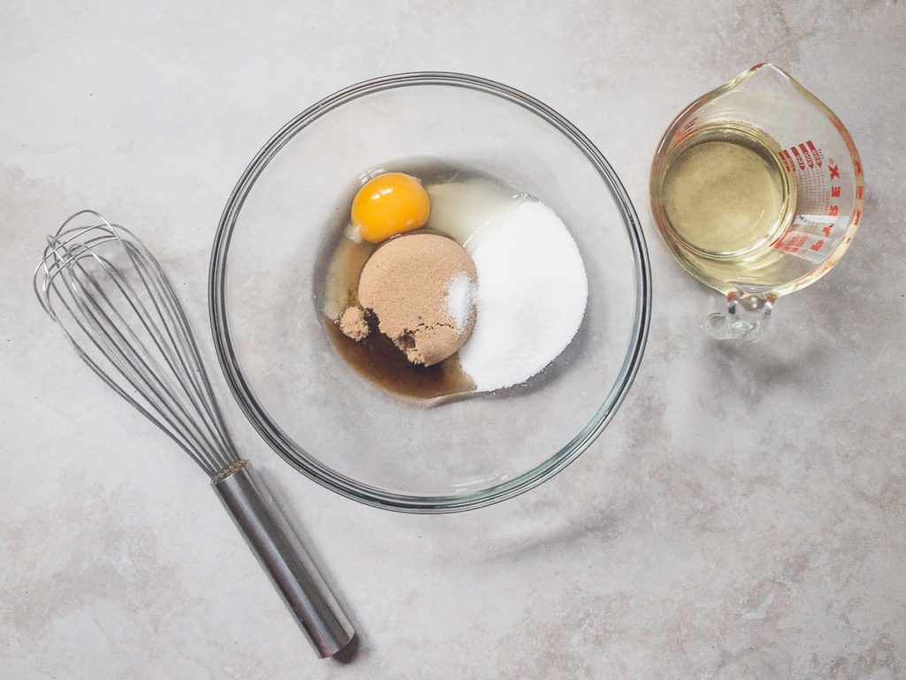 whisk, glass bowl with sugars and egg, liquid measuring cup with oil