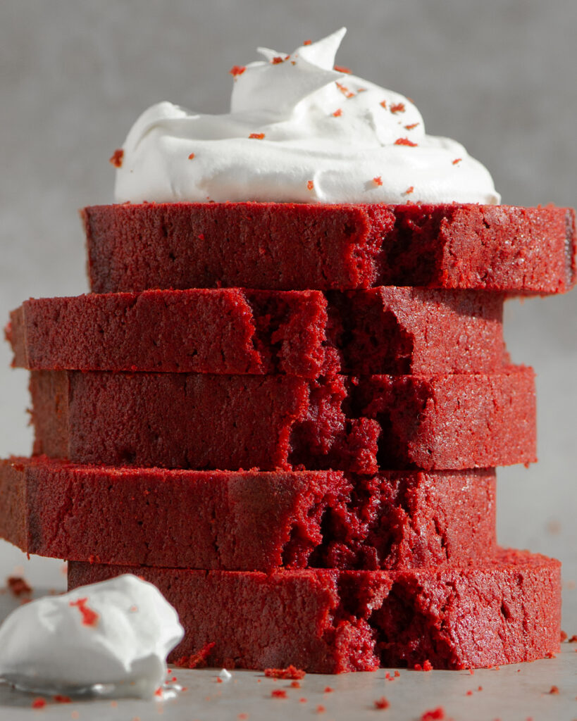 stacked slices of red velvet loaf cake topped with whipped cream