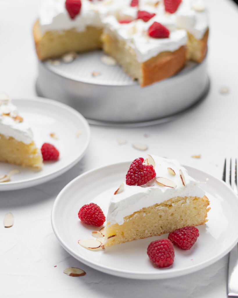 A slice of almond pound cake topped with whipped cream, sliced almonds, and fresh raspberries.
