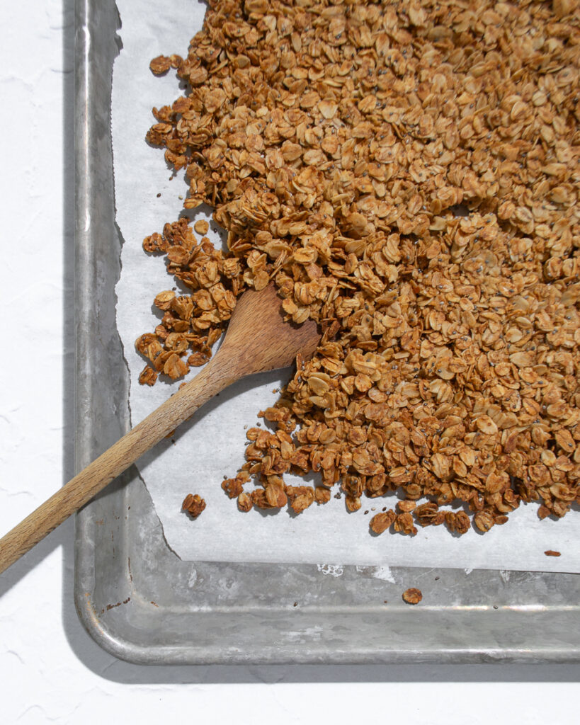 Fresh baked granola being broken up into toasted, crunchy clusters.