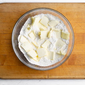 Cold slices of unsalted butter have been added to the scone dry ingredients and are ready to be cut into the flour.