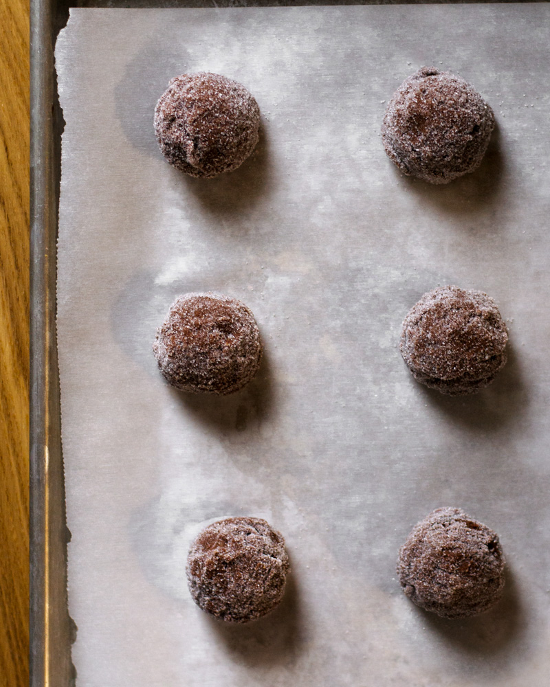 Chocolate sugar cookie dough, rolled in a thin layer of granulated sugar and waiting on a lined baking tray before baking in the oven.