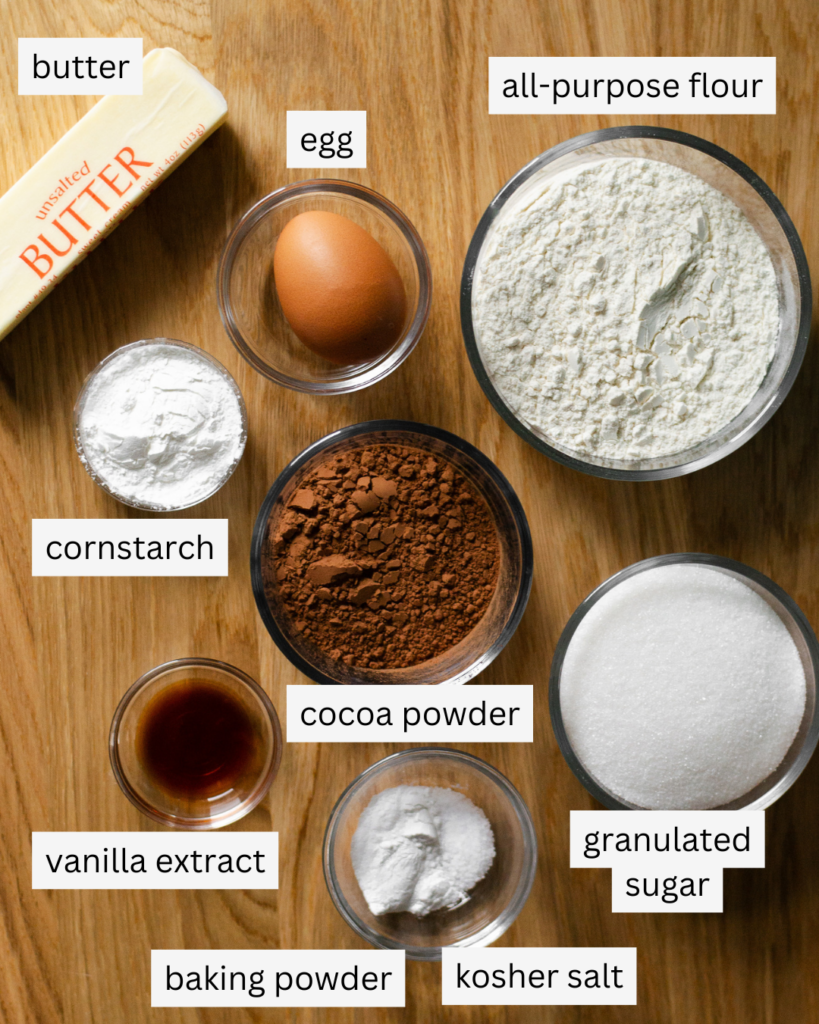 Ingredients to be used in a recipe for chocolate sugar cookies: unsalted butter, a large egg, cornstarch, all-purpose flour, cocoa powder, vanilla extract, baking powder, kosher salt, and granulated sugar.