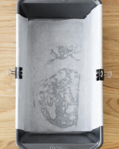 A greased large bread pan lined with parchment paper, prepped for broiled cinnamon shortbread bars.