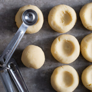 Dough for vanilla thumbprint cookies, using the back of a rounded teaspoon to make a well or divot in the middle of the cookies, to later fill with chocolate ganache.